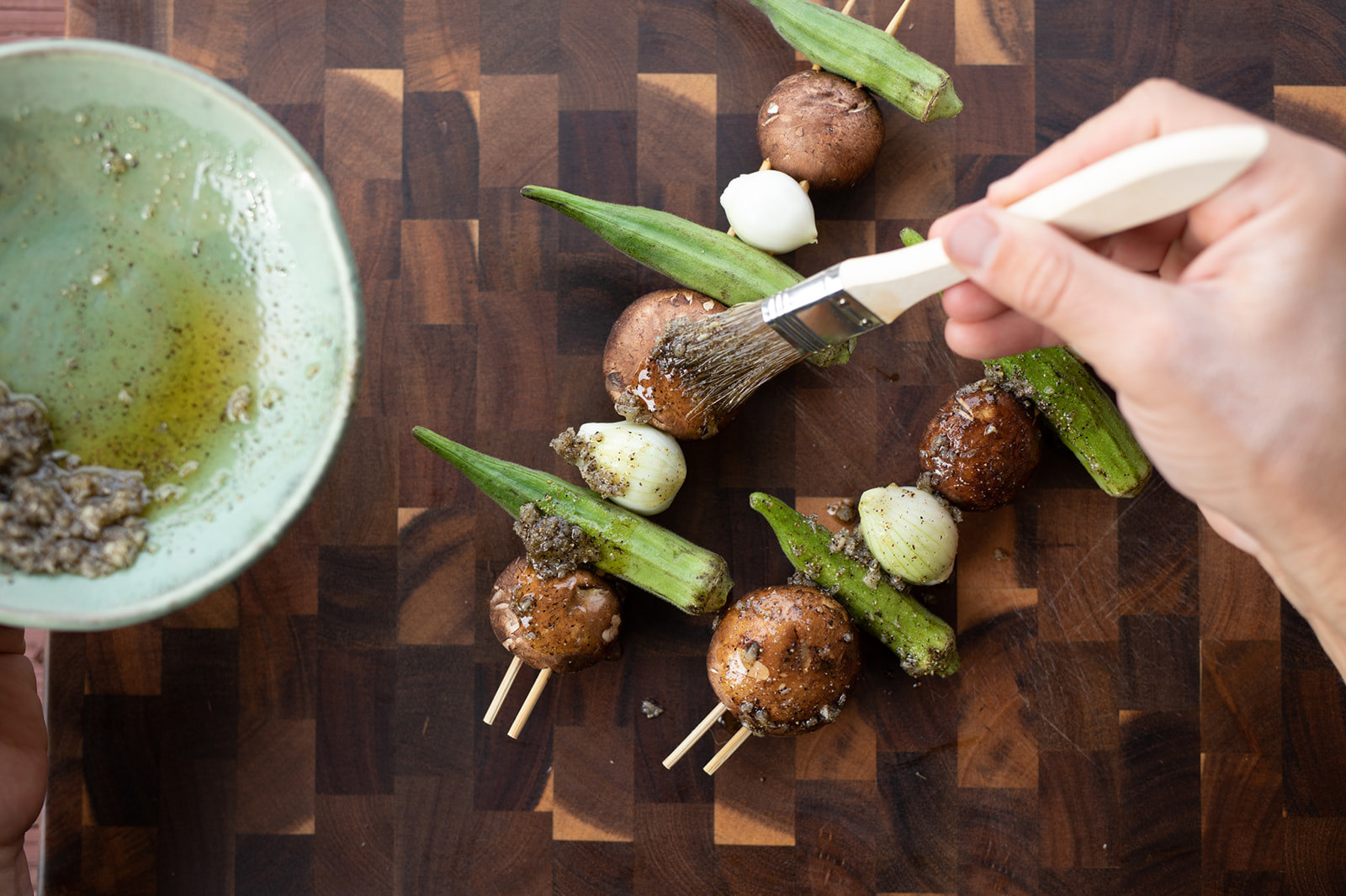 Brushing mushrooms and okra kabobs with oil and seasonings.