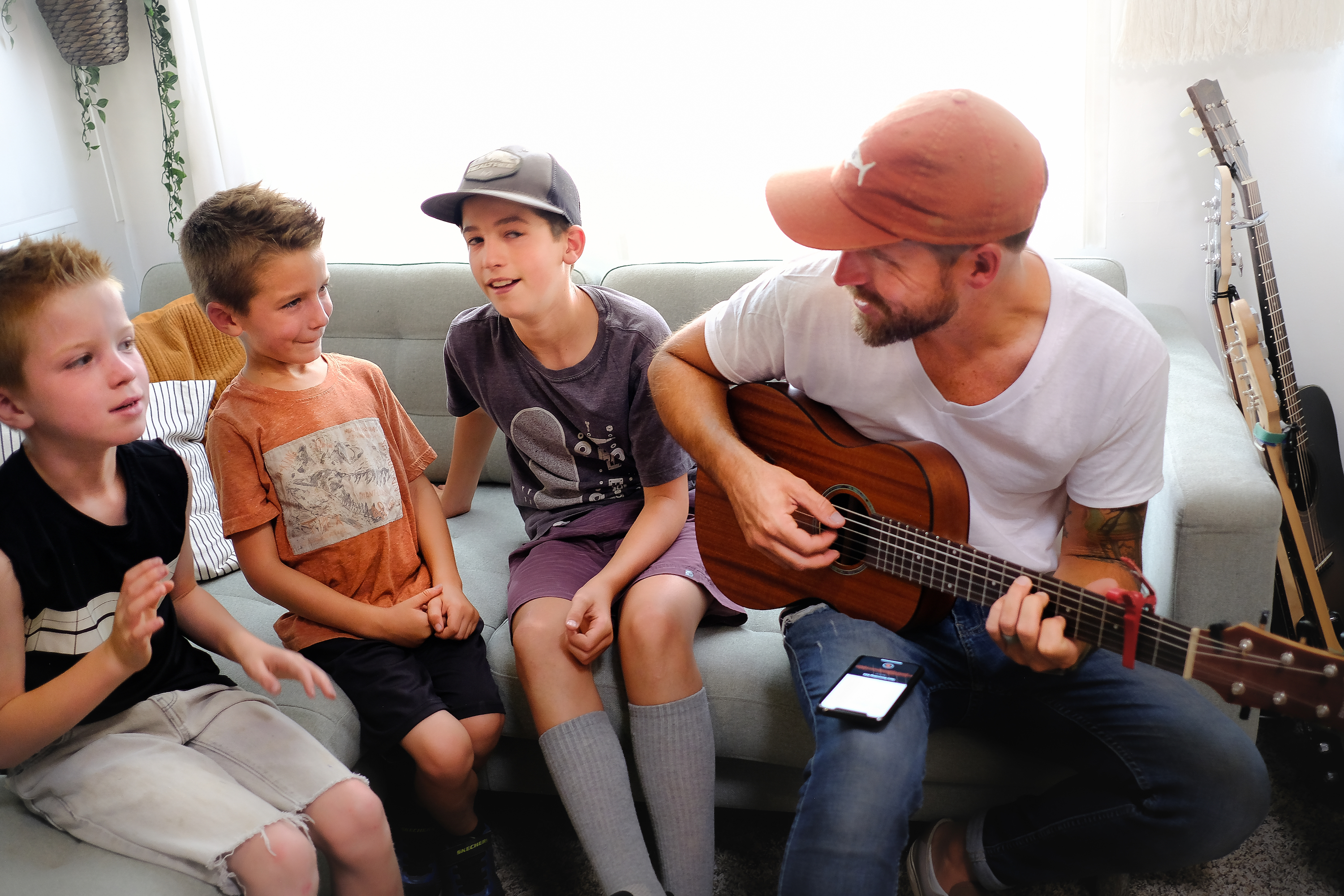 Amick Cutler plays guitar while his three sons sing along while sitting on a couch in their RV.