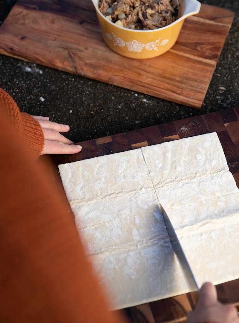 Cutting pastry dough into equal squares on a cutting board.