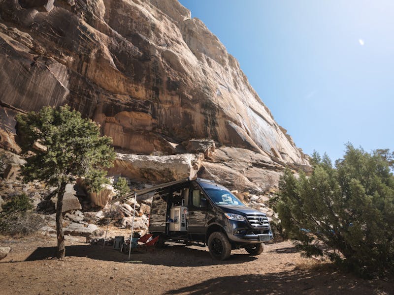A Thor Motor Coach Sanctuary parked at a campsite next to a rocky mountainside.