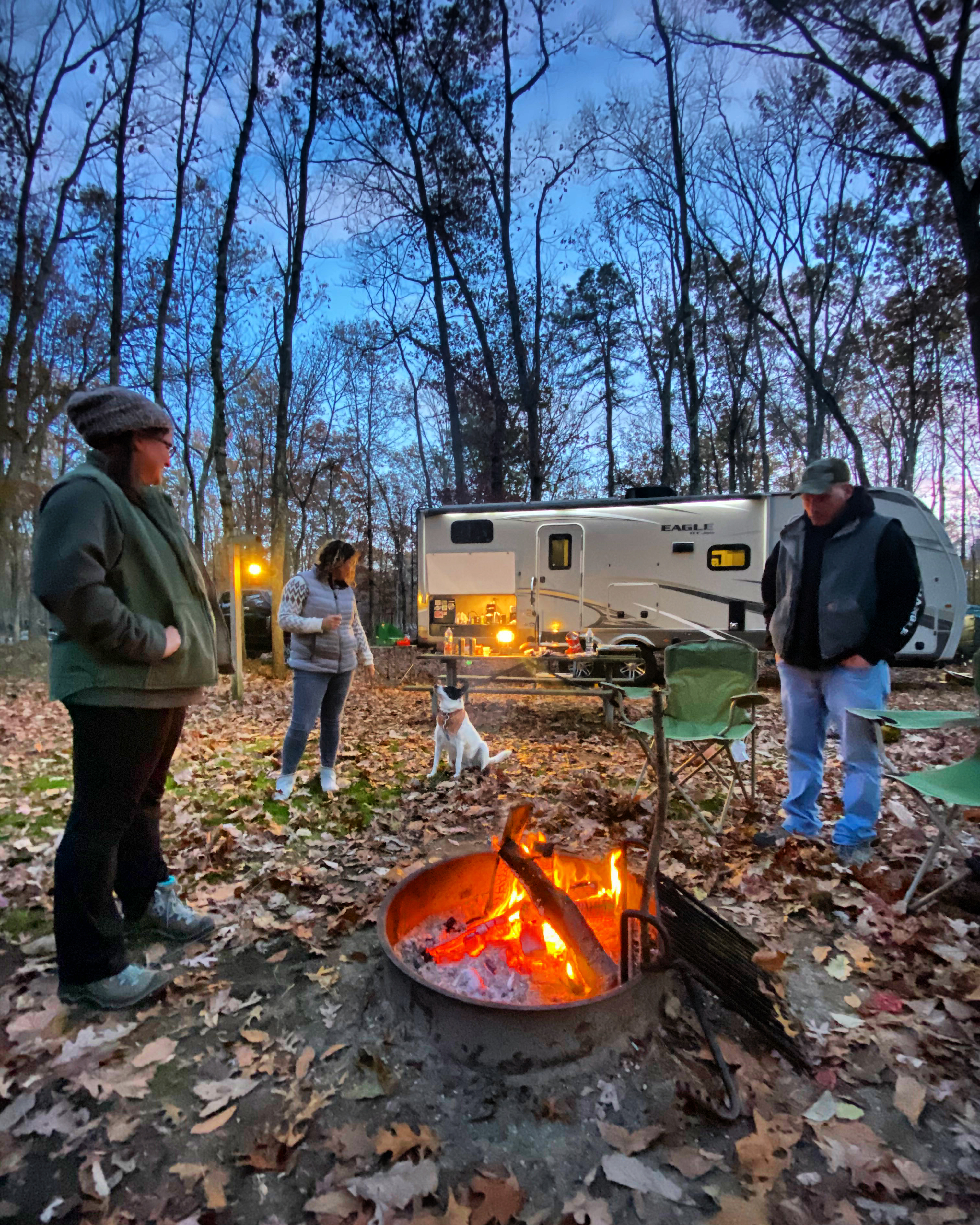 Three adults around a campsite fire pit, social distancing. 