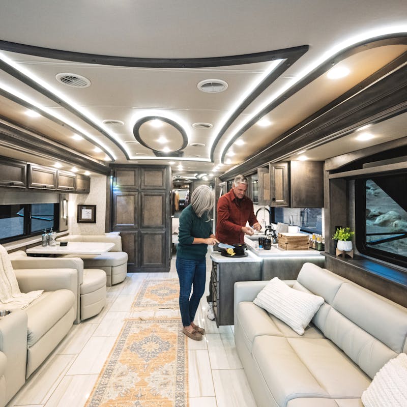 A man and women prepare tea at the kitchen counter inside of an Allegro Bus