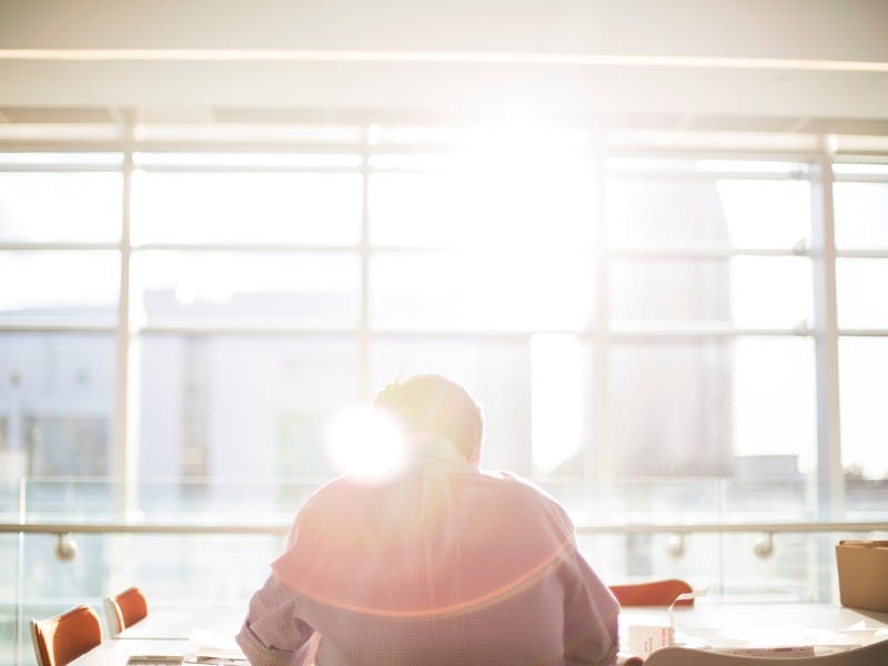 man sits alone at a table by window with sun streaming in