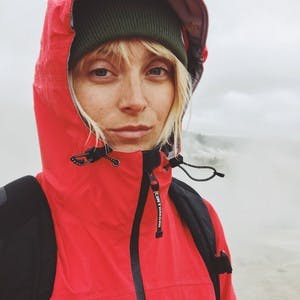 Laura Jayne Austin, wearing a beanie and a red jacket with her hood up, slightly smiles at the camera.