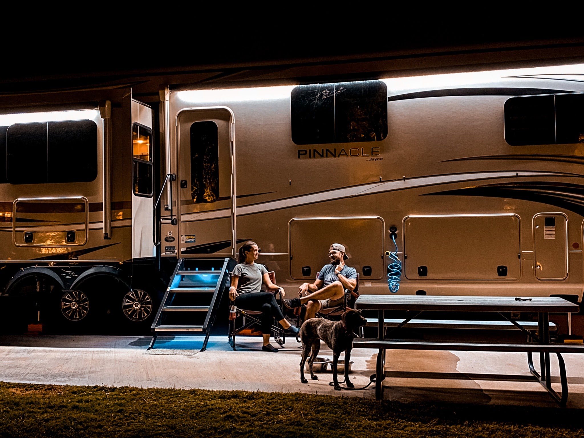 Holly Miner and her husband sitting in front of their Jayco Pinnacle at night.