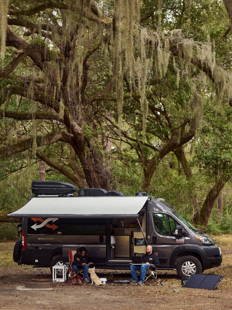 Gabe and Rocio sitting outside of their RV under a large oak tree
