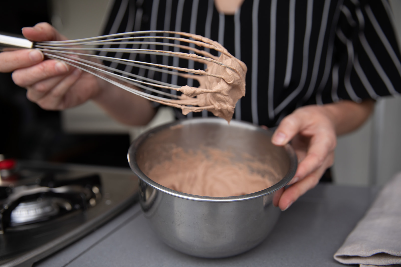 A woman holding a whisk up to show the chocolate whipped cream she's just prepared.