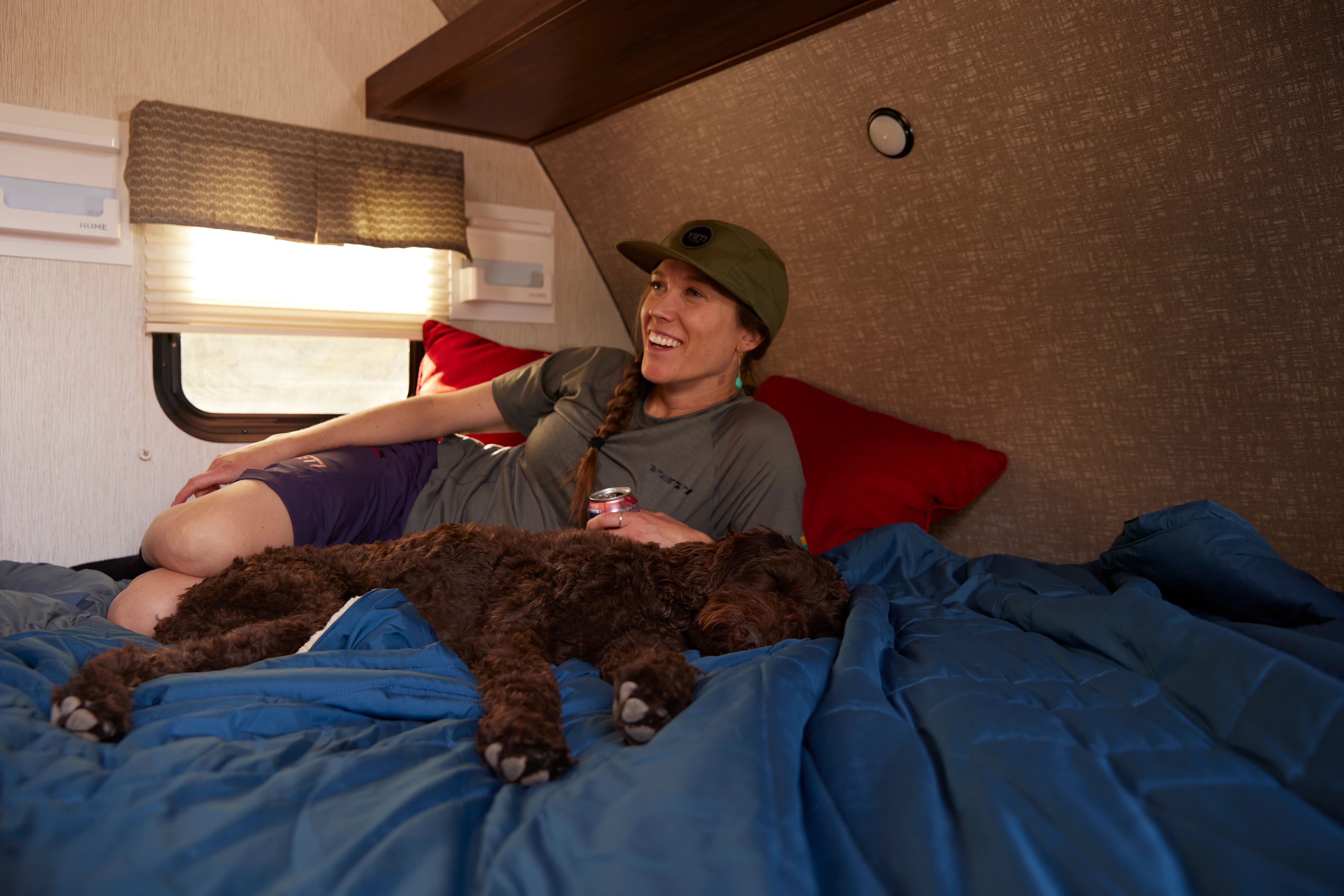 Britt Greer lays on the bed inside a travel trailer with her dog