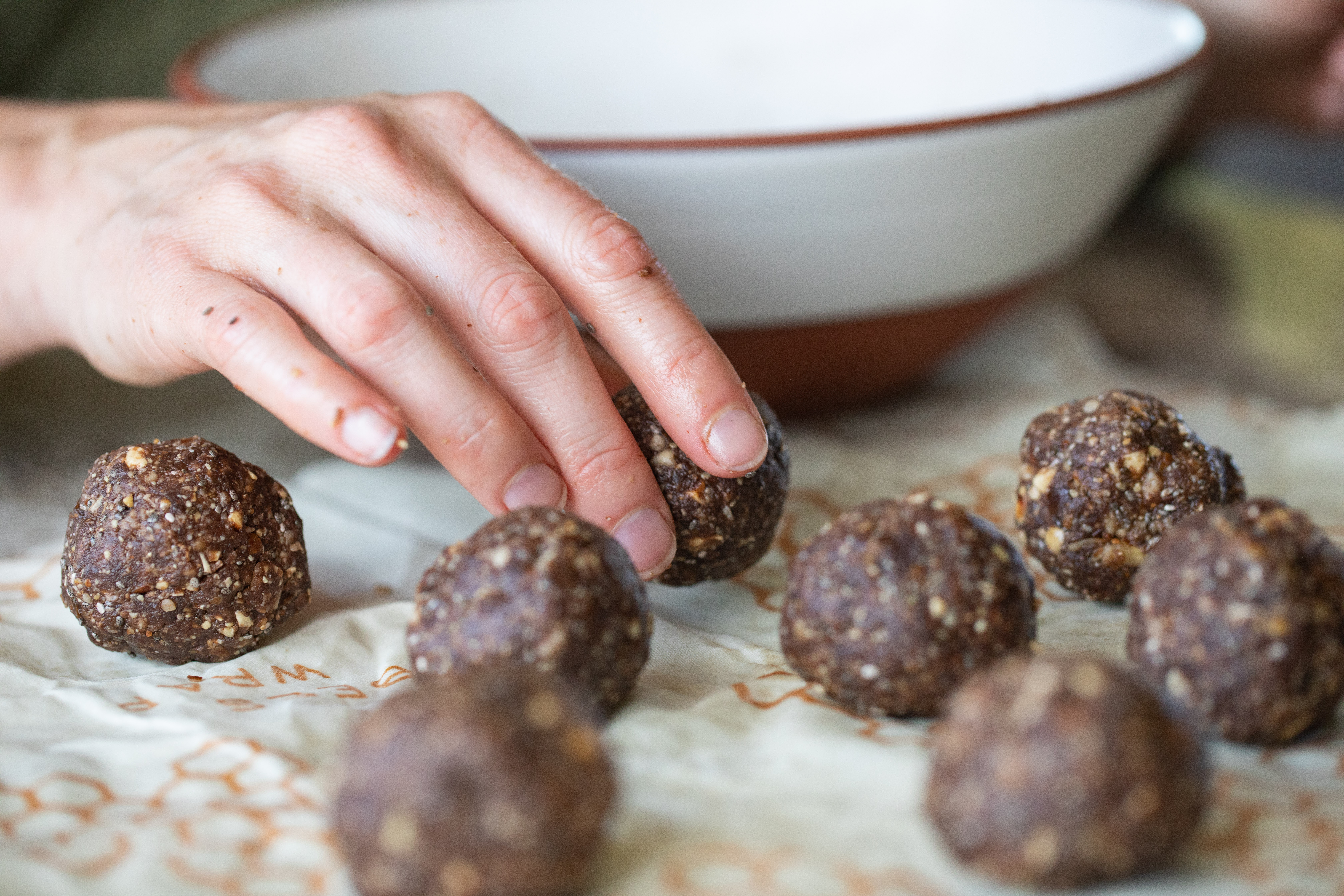 A hand reaching for a Chia Power Bliss Ball on a table. 