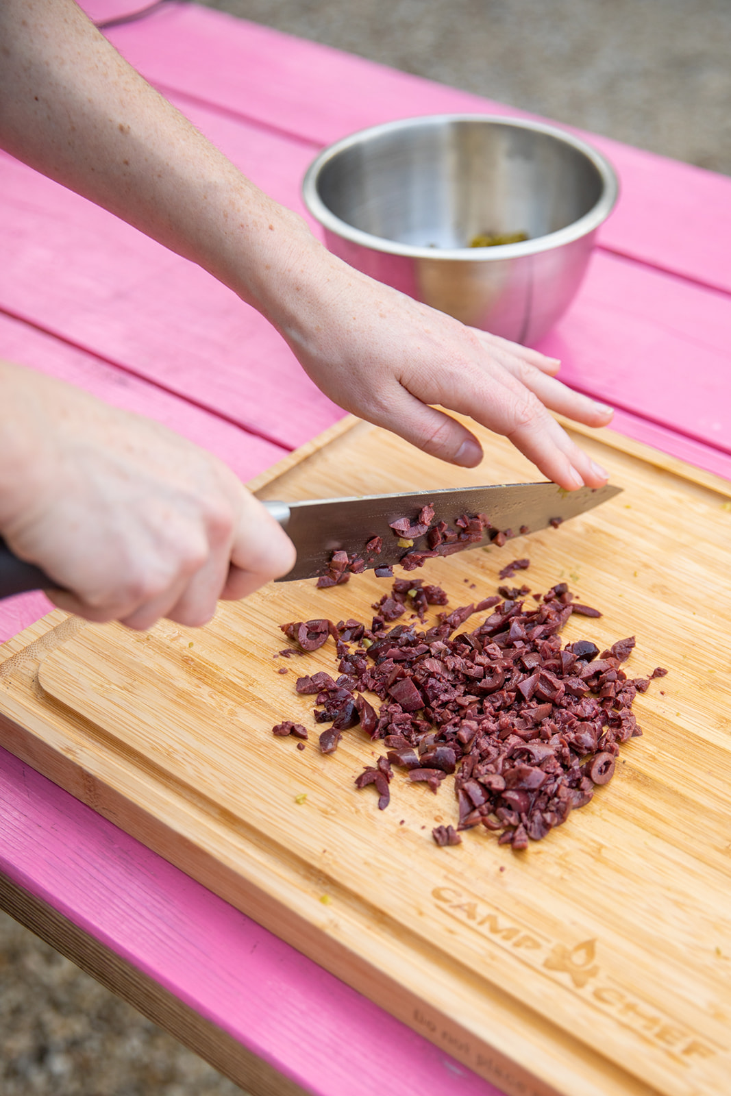 Hands holding a knife above chopped olives on a cutting board. 