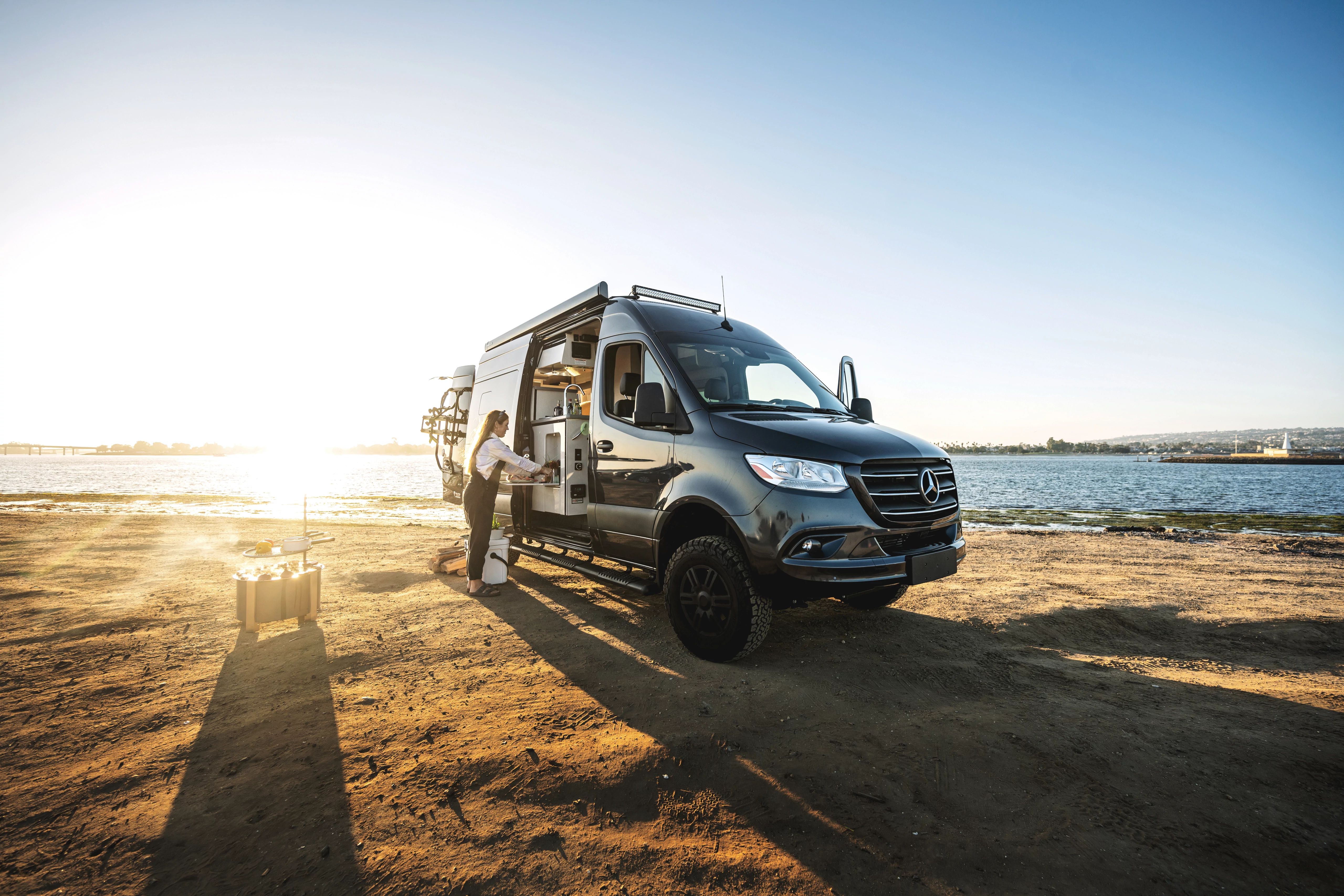 Sarah Glover preparing a meal out of the side of a class B Camper Van by the ocean
