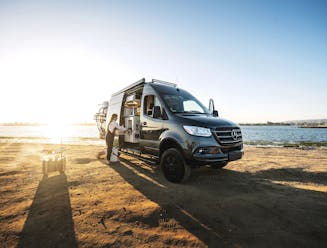 Sarah Glover preparing a meal out of the side of a class B Camper Van by the ocean