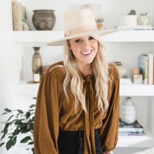 A headshot of Amber Thrane posed against a white wall of shelves filled with knick-knacks.
