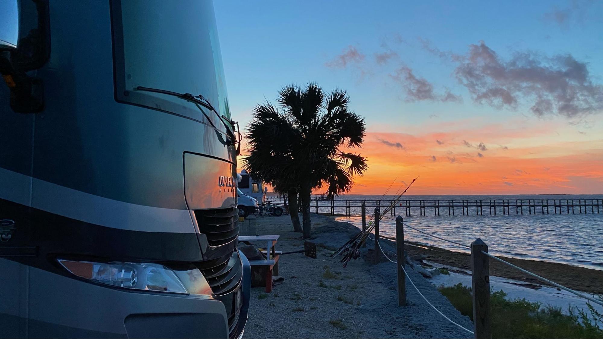 Michael and Tiffany Dunagan's Tiffin Allegro RV parked at a waterfront beach campsite at sunset.