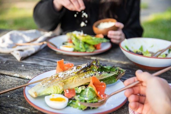 Caesar salad with grilled asparagus, soft-boiled egg, and lox on a plate while man holds fork about to eat salad.