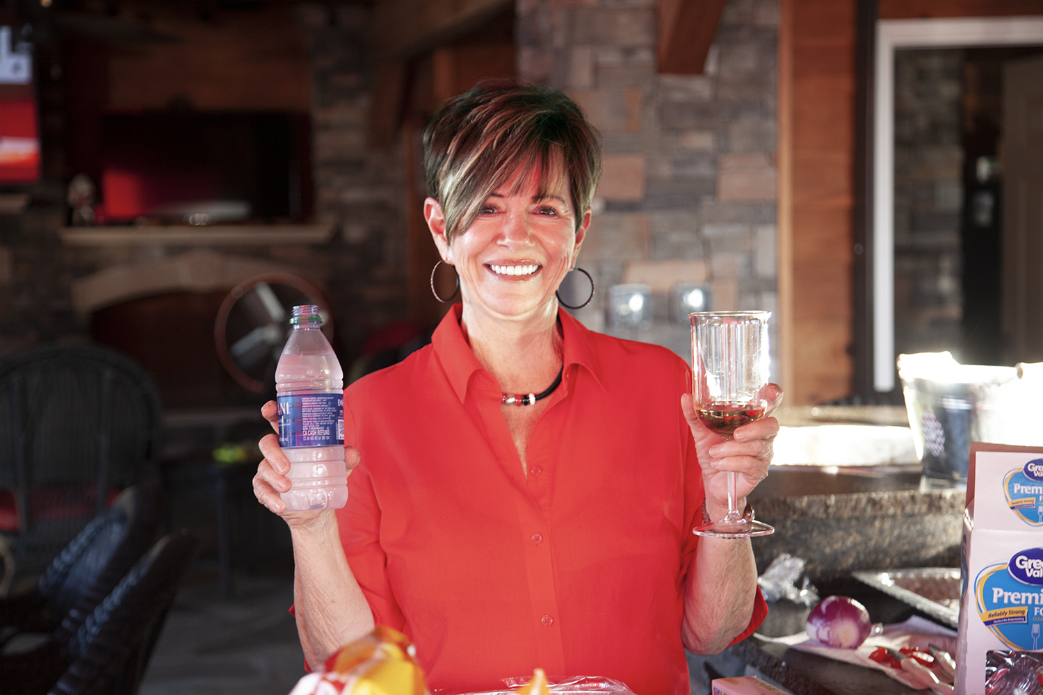 A woman holding an alcoholic beverage in one hand and a bottle of water in the other, on display for the camera.