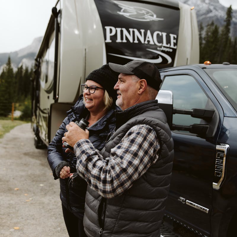 A couple using binoculars in front of an RV
