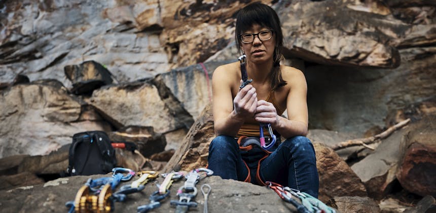 Kathy Karlo holding up climbing gear while sitting on a rock