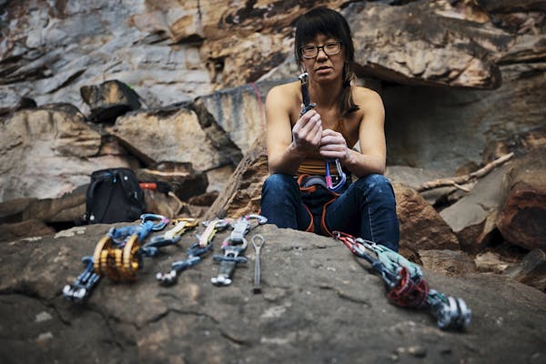 Kathy Karlo holding up climbing gear while sitting on a rock