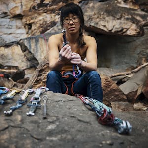 Kathy Karlo holding up climbing gear while sitting on a rock