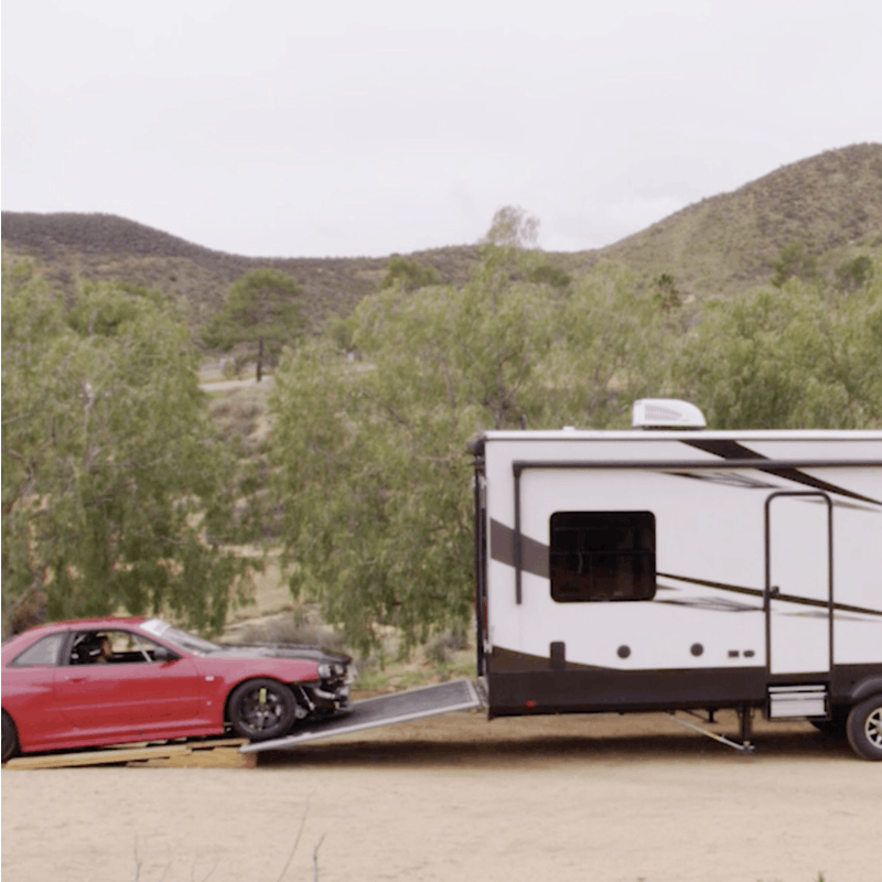 A pickup truck hauling a Highlander Toy Hauler while a racecar is loaded in the toy hauler.