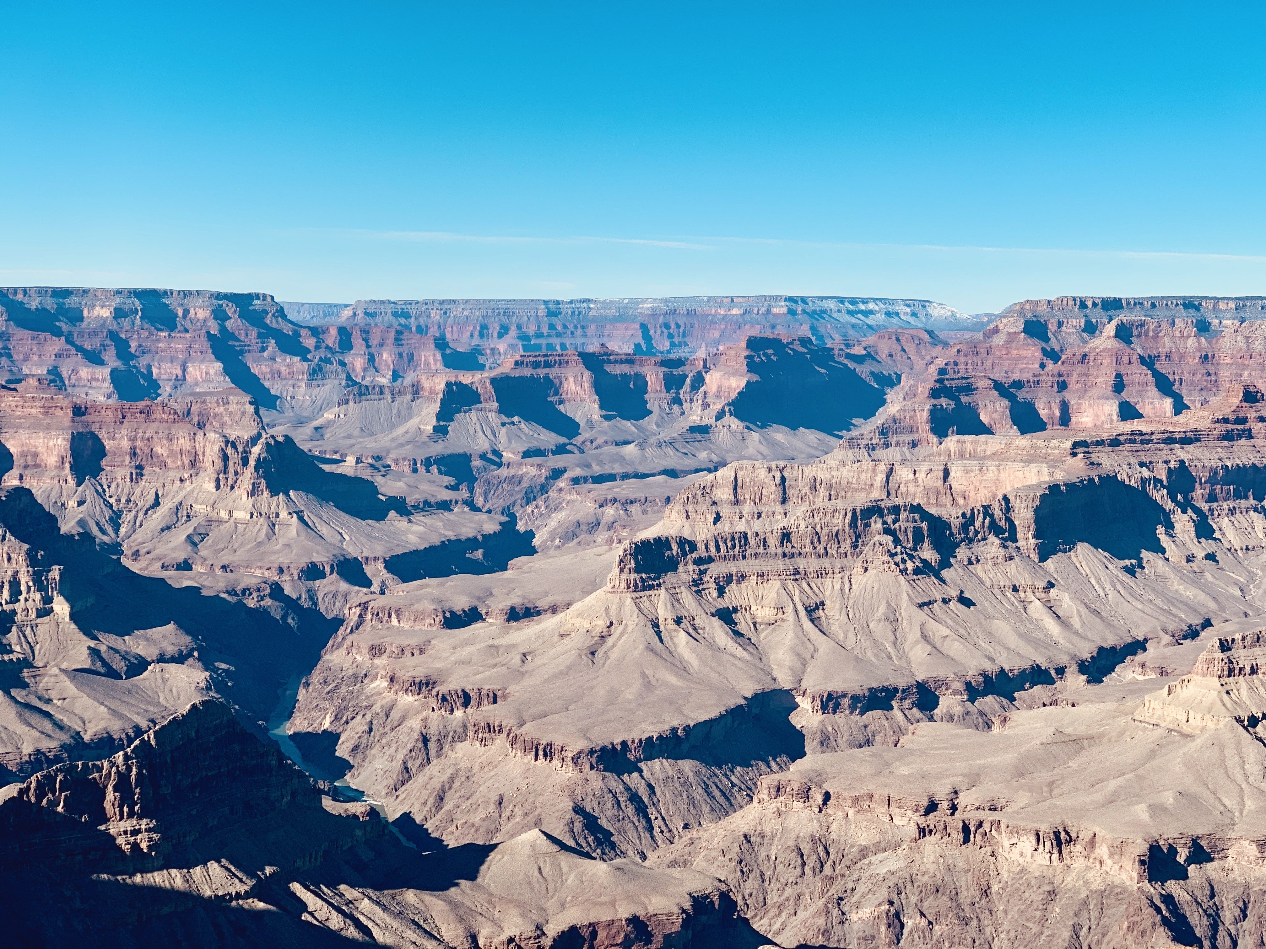 Expansive shot of the Grand Canyon with bright blue skies and views of Colorado River