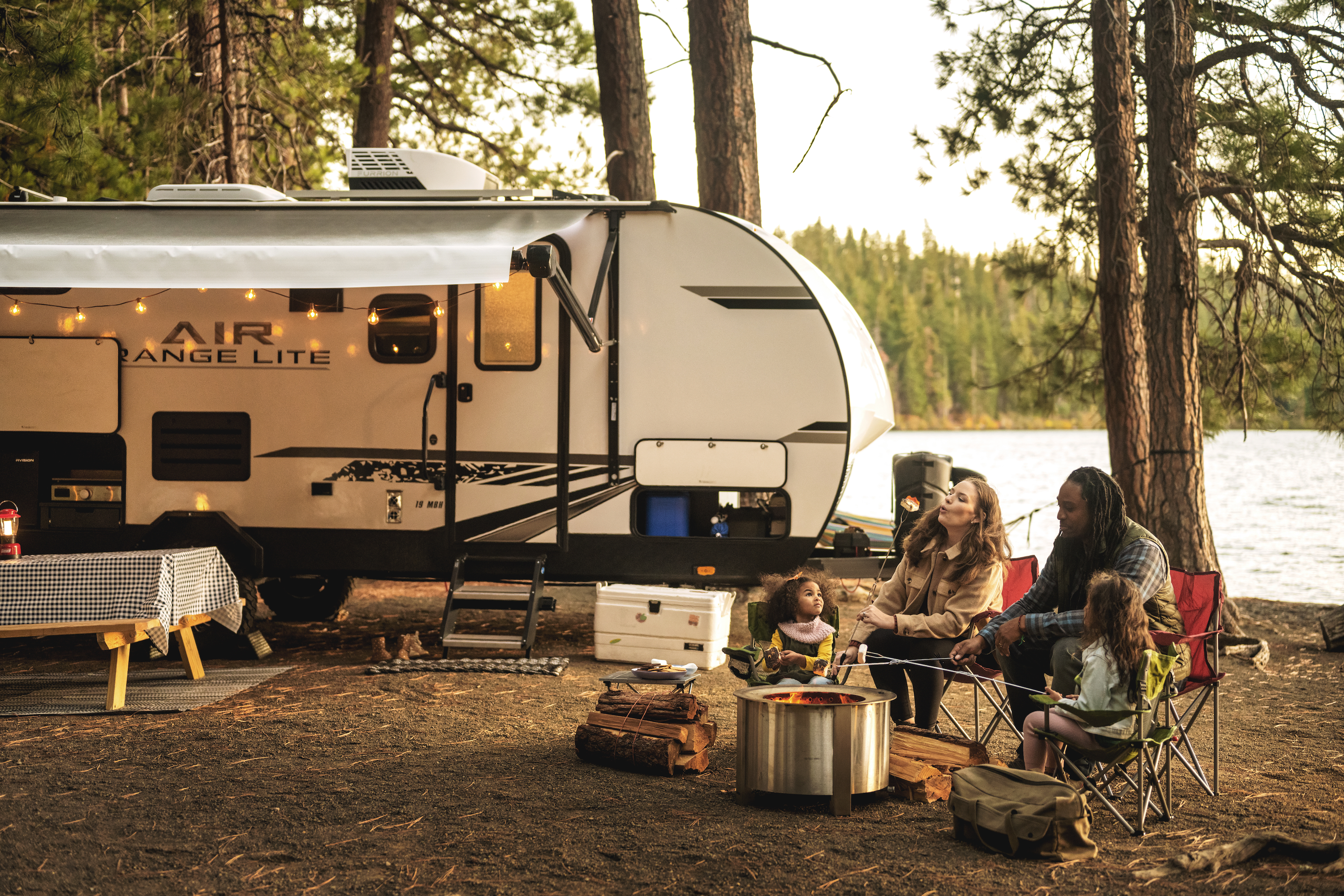 A family sits around a fire making smores with an RV in the background