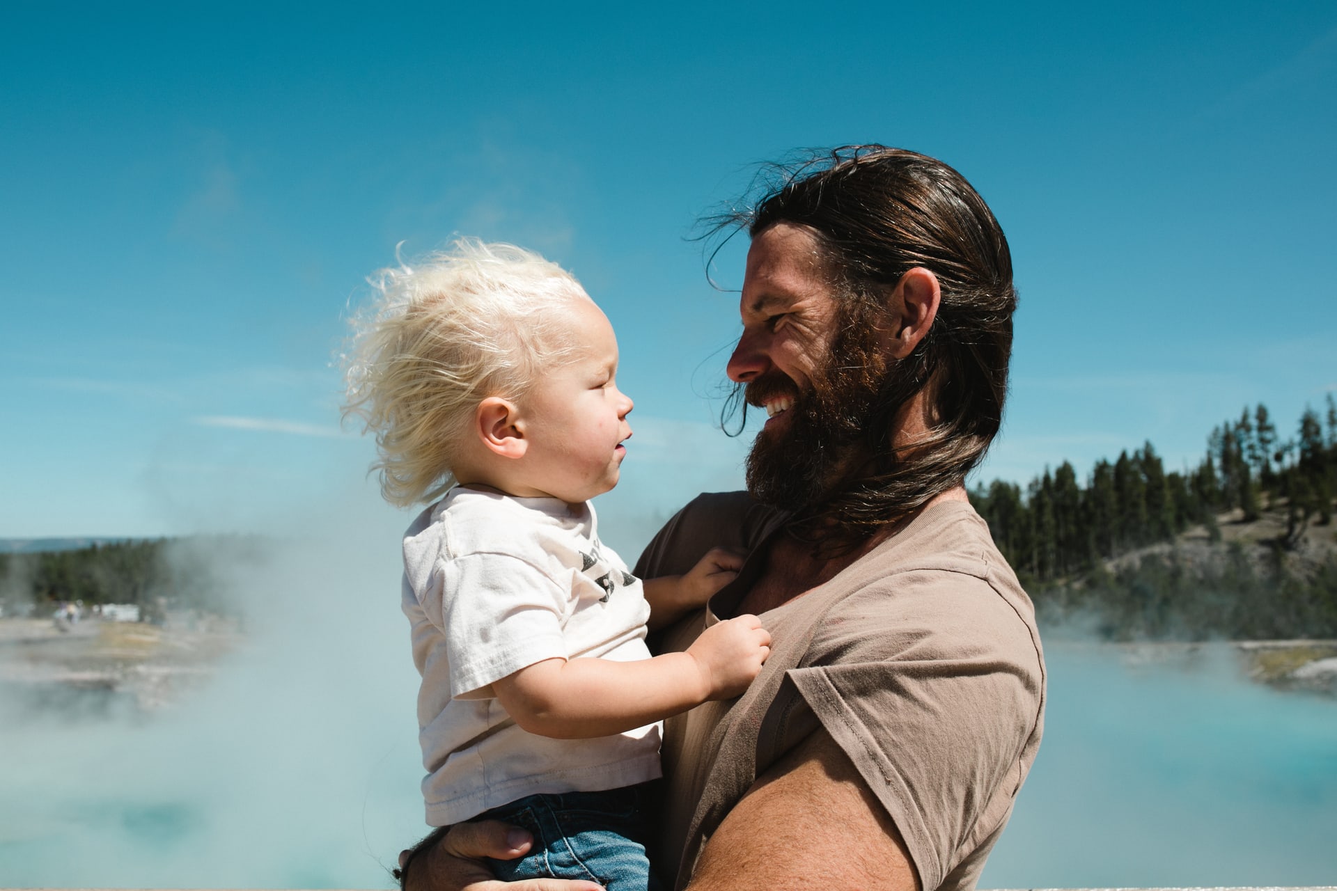 Father holds son and looks at each other in front of steaming hot springs