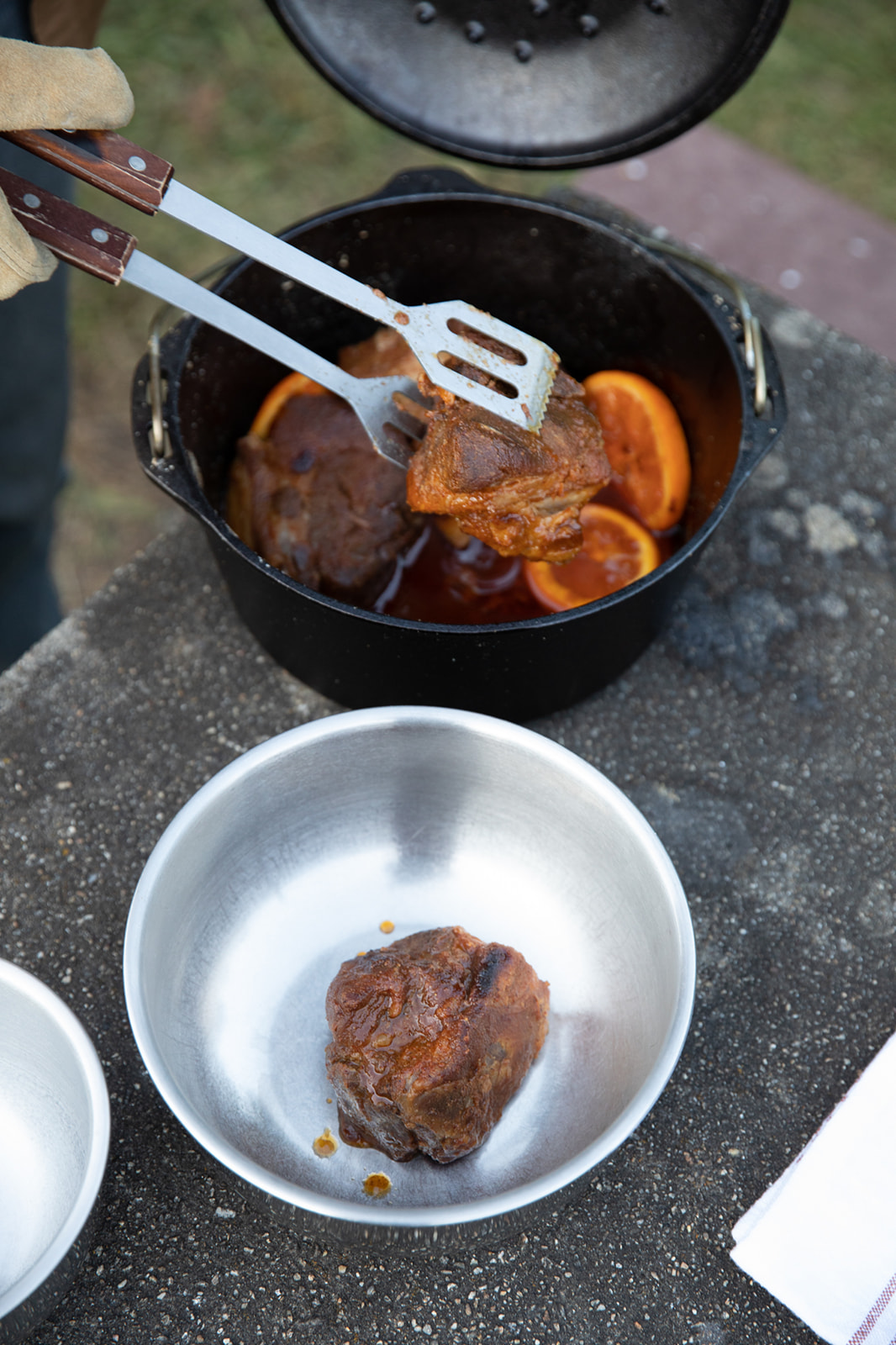 A pair of tongs pulls out cooked pieces of pork from a Dutch oven.