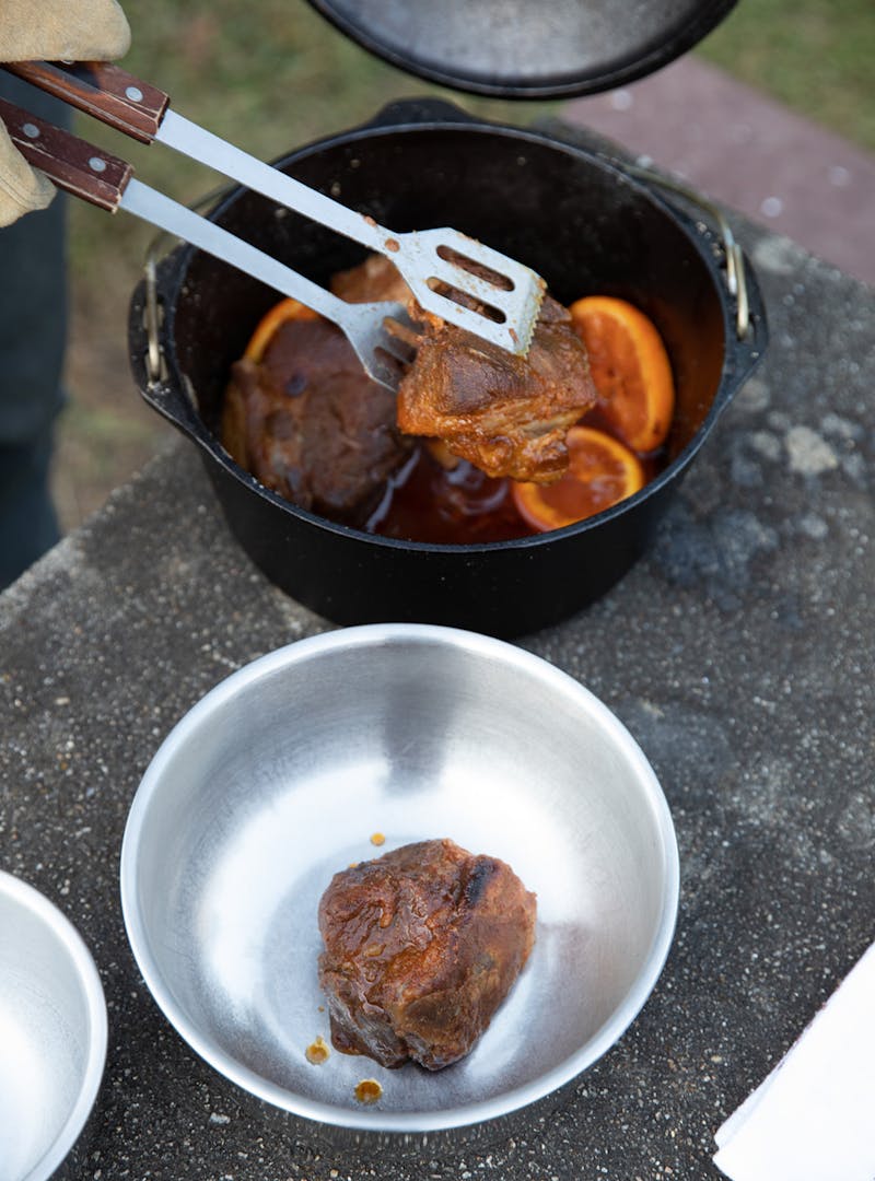 A pair of tongs pulls out cooked pieces of pork from a Dutch oven.