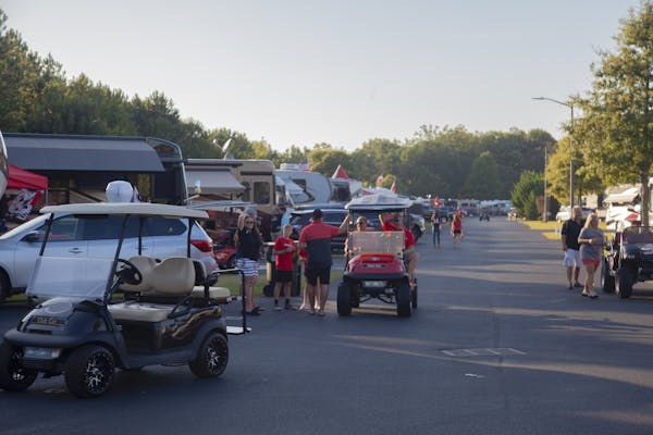 A shot of a golf cart driving down a road lined with dozens of RVs at a tailgating RV park.