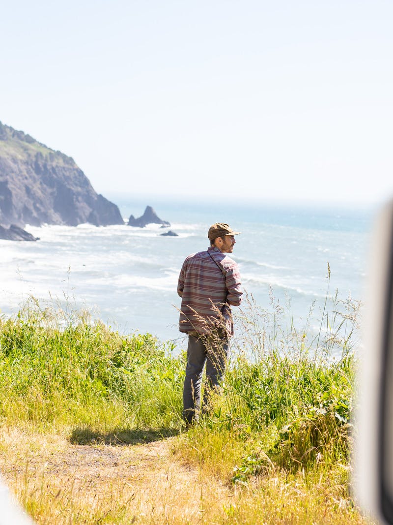 Man with beard stands outside of RV door and looks out onto the Pacific Ocean off of the Pacific Coast Highway in Southern Oregon.