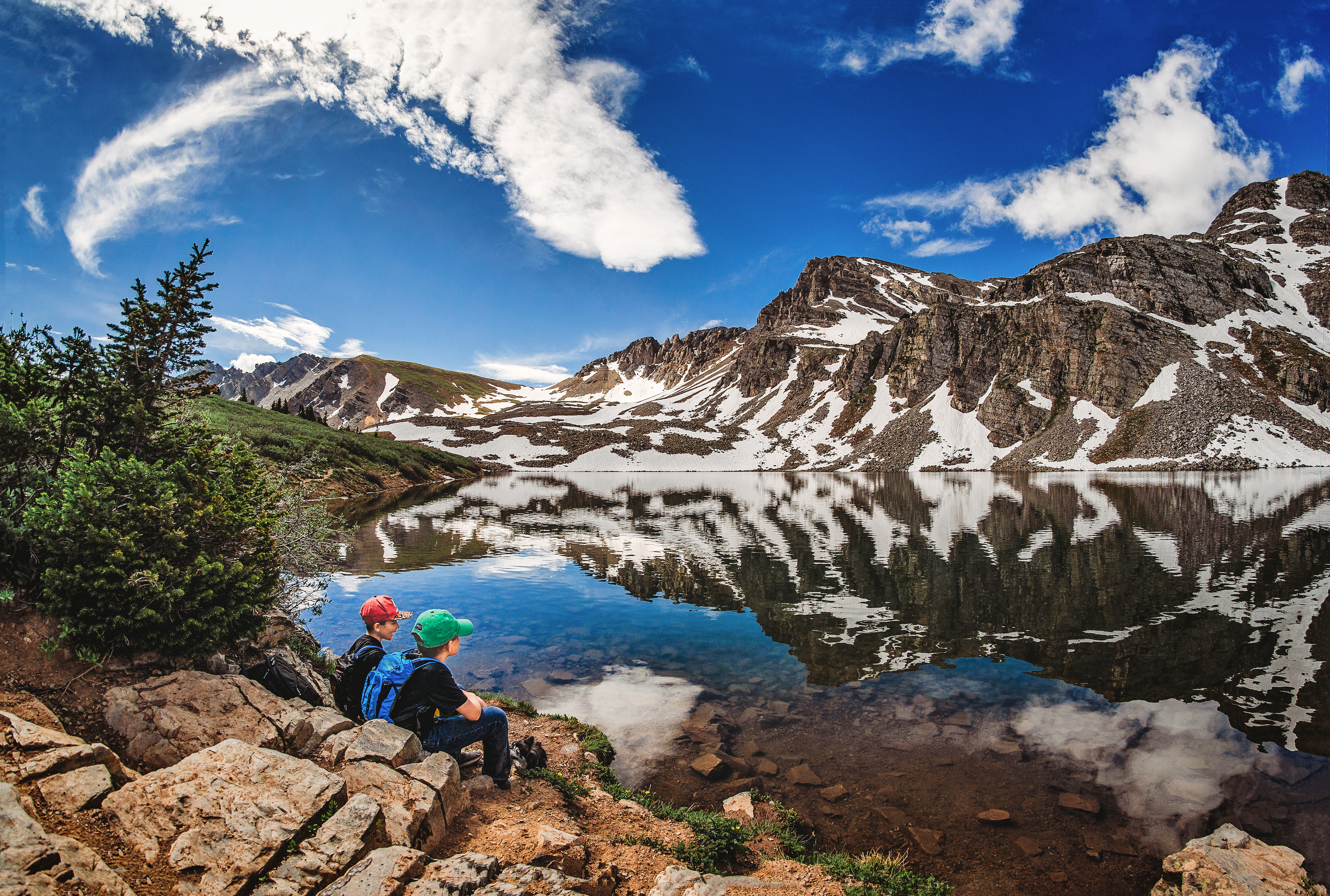 Alison Takacs's children sit by a lake with mountains in background.