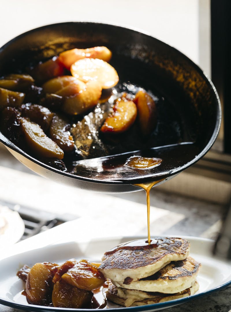 Peach liquid being poured over plate of mini pancakes.