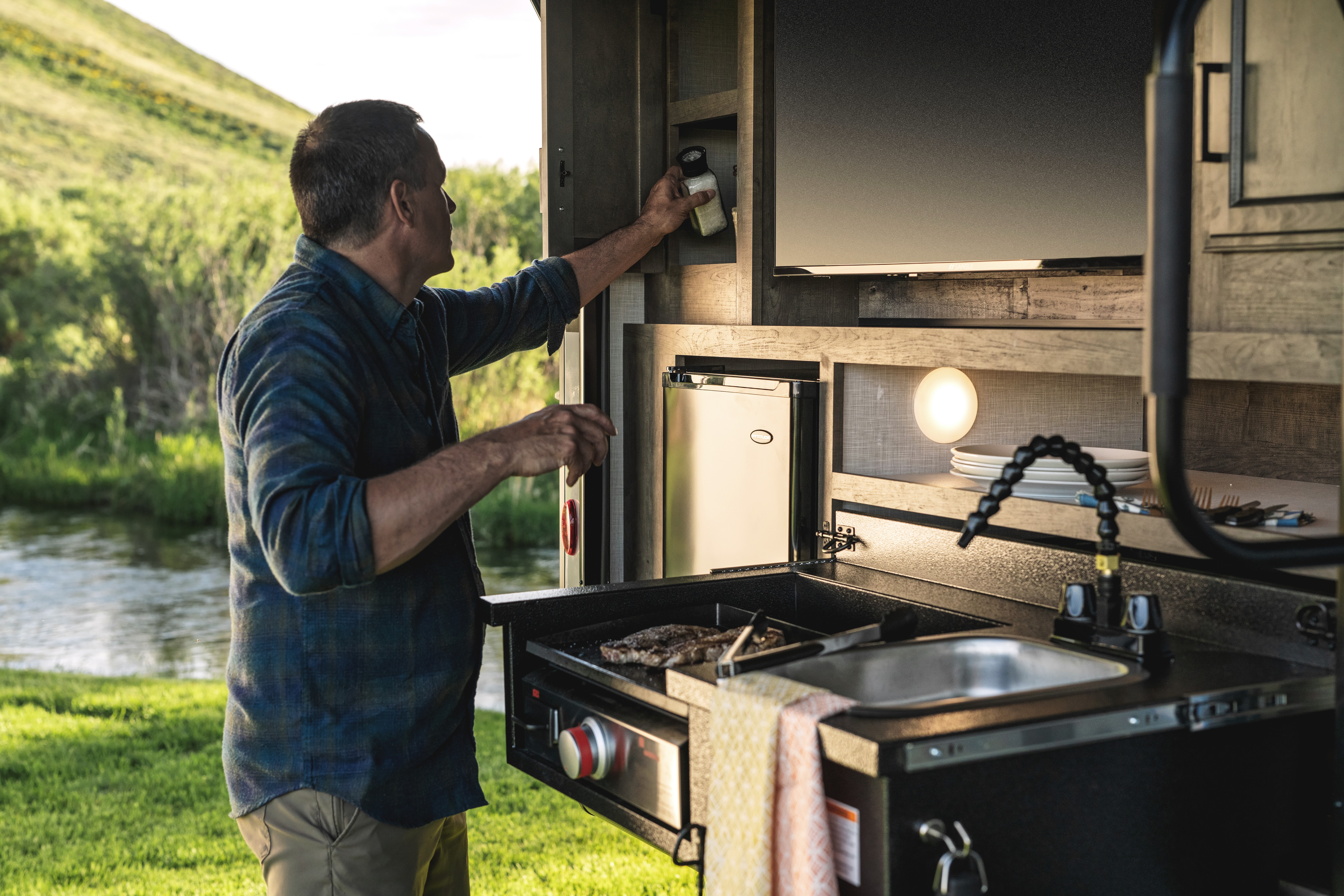 A man puts salt away in a cabinet on the exterior of a KZ Venture Stratus.