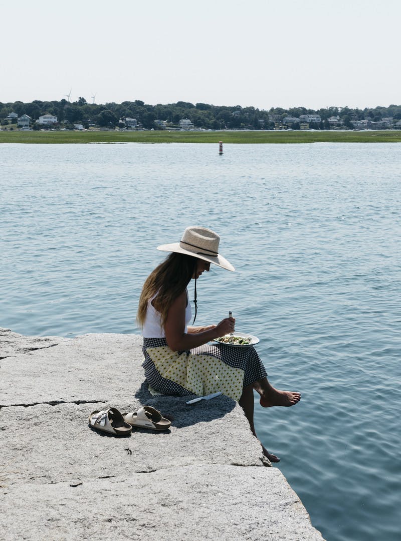Sarah sitting on a pier, legs dangling over, eating her lunch. 