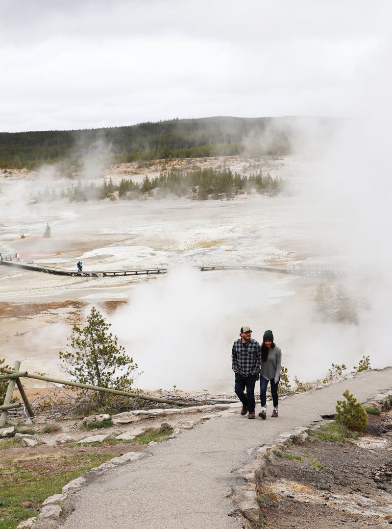 Juli and Jordan Cote walking down dirt path to steaming geysers in Yellowstone National Park.