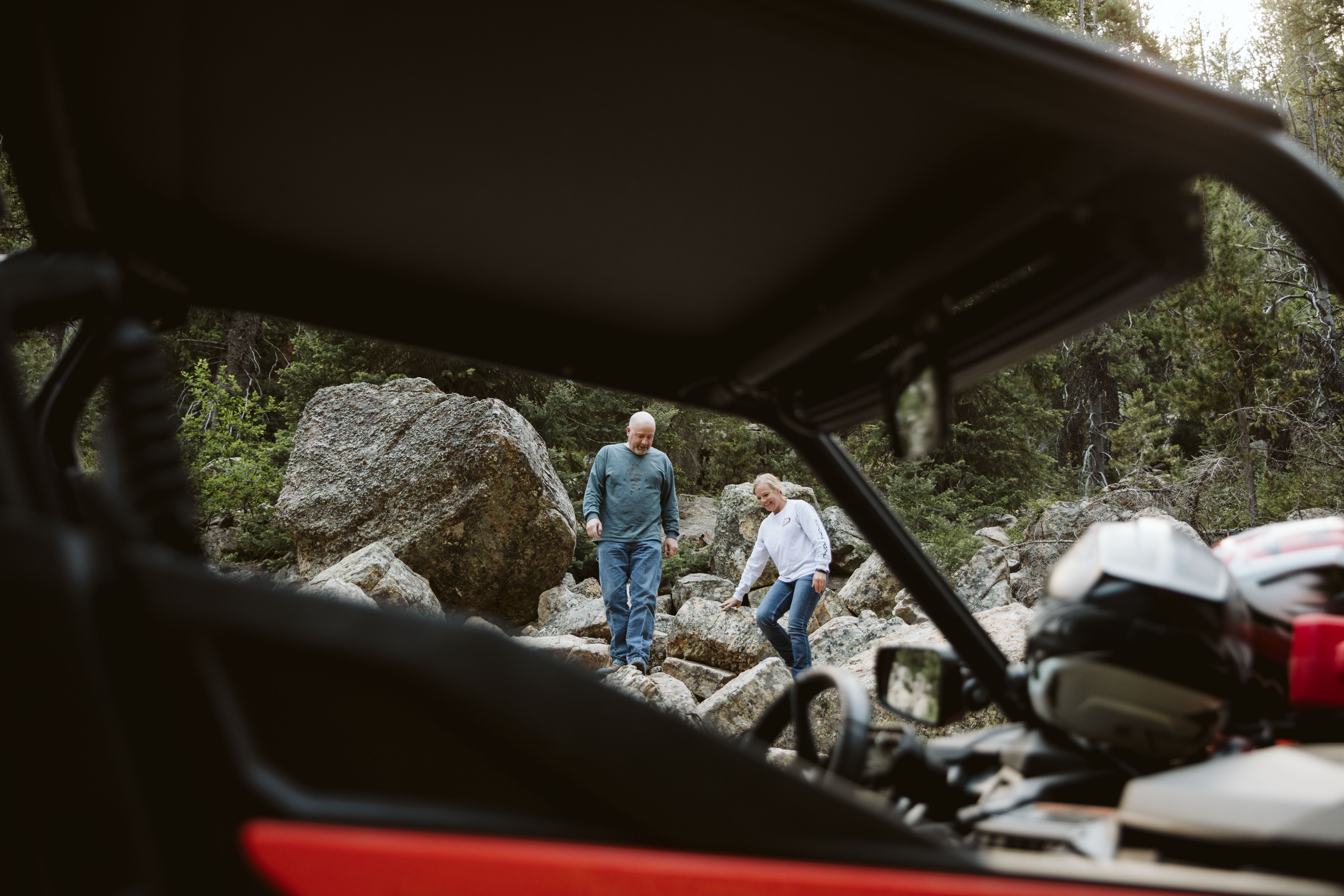 A couple climbs down rocks towards their side by side.