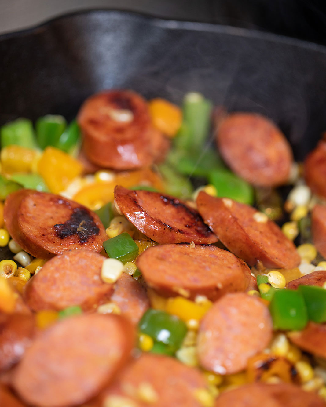 A close-up shot of sausage and vegetables cooking in a skillet. 