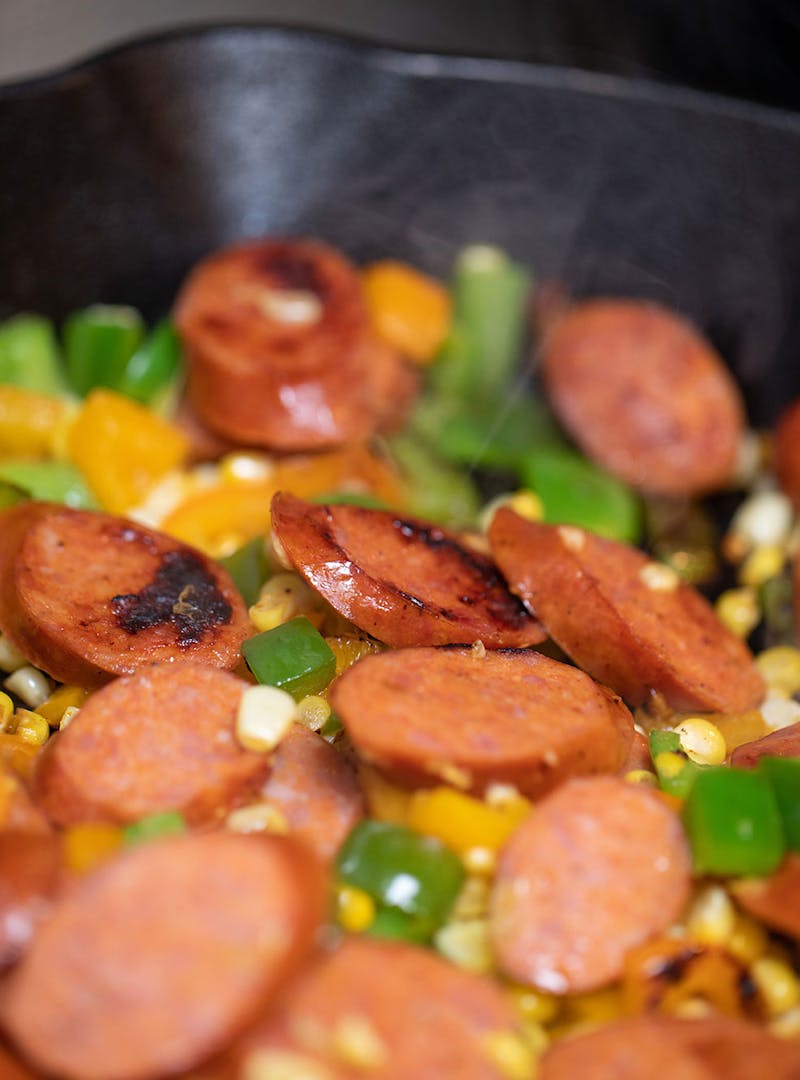 A close-up shot of sausage and vegetables cooking in a skillet.