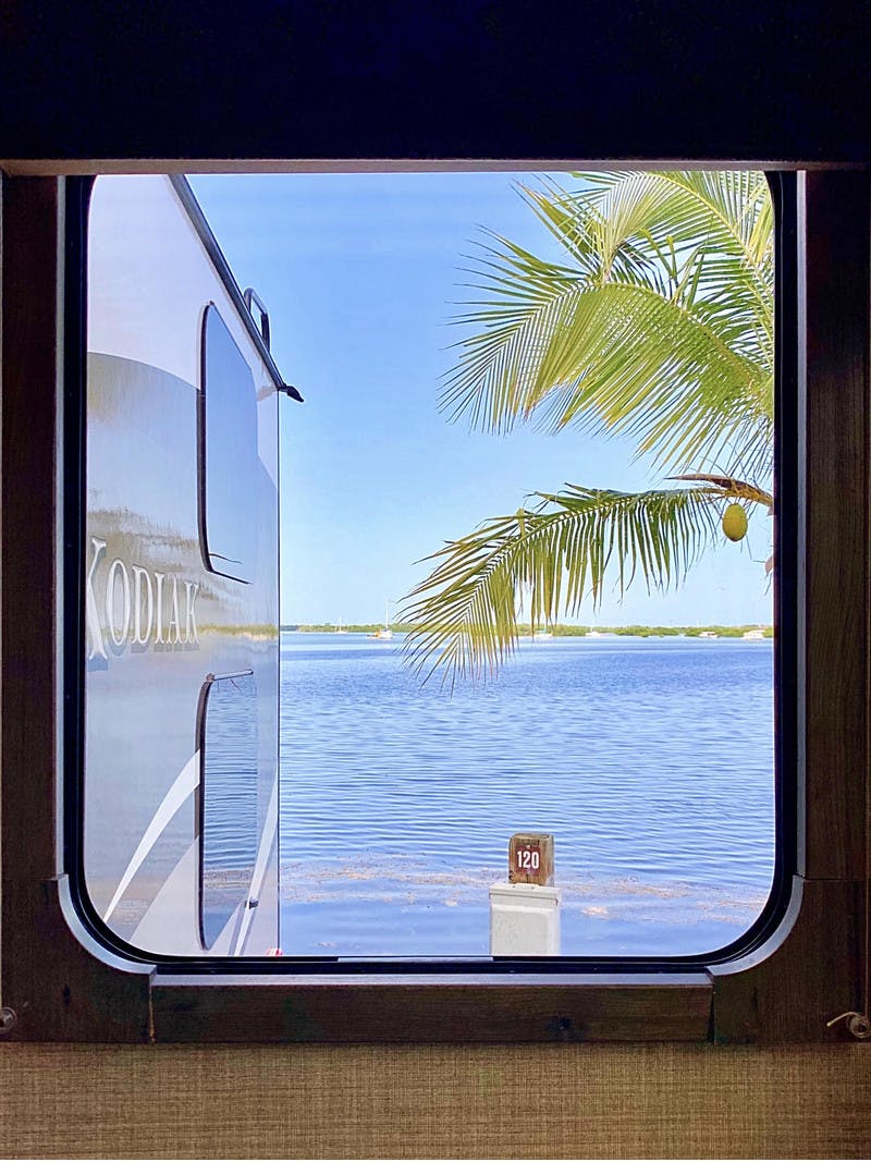 Window To The World Dutchmen Kodiak RV view looking out to the ocean with a palm tree in Key West, Florida.