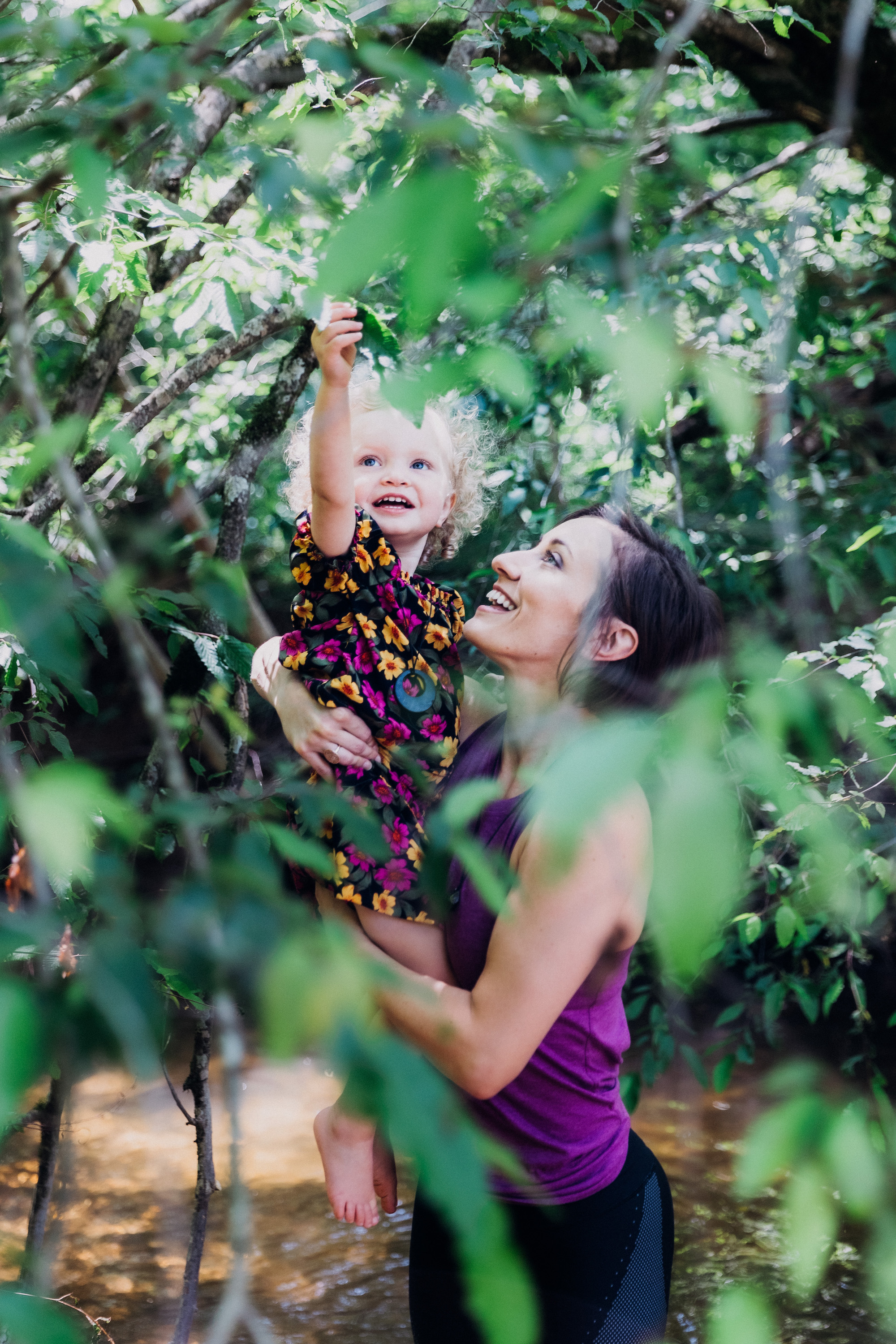 A young mom and her daughter examining a leaf in nature together.