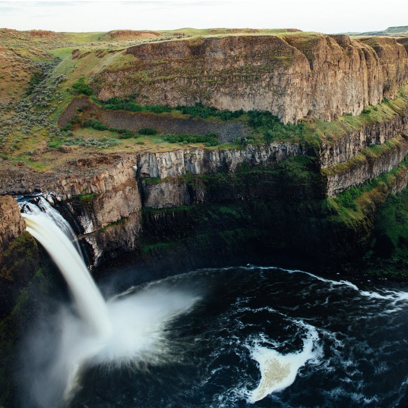 A beautiful waterfall in Washington falling into a stream with beautiful greenery surrounding it.
