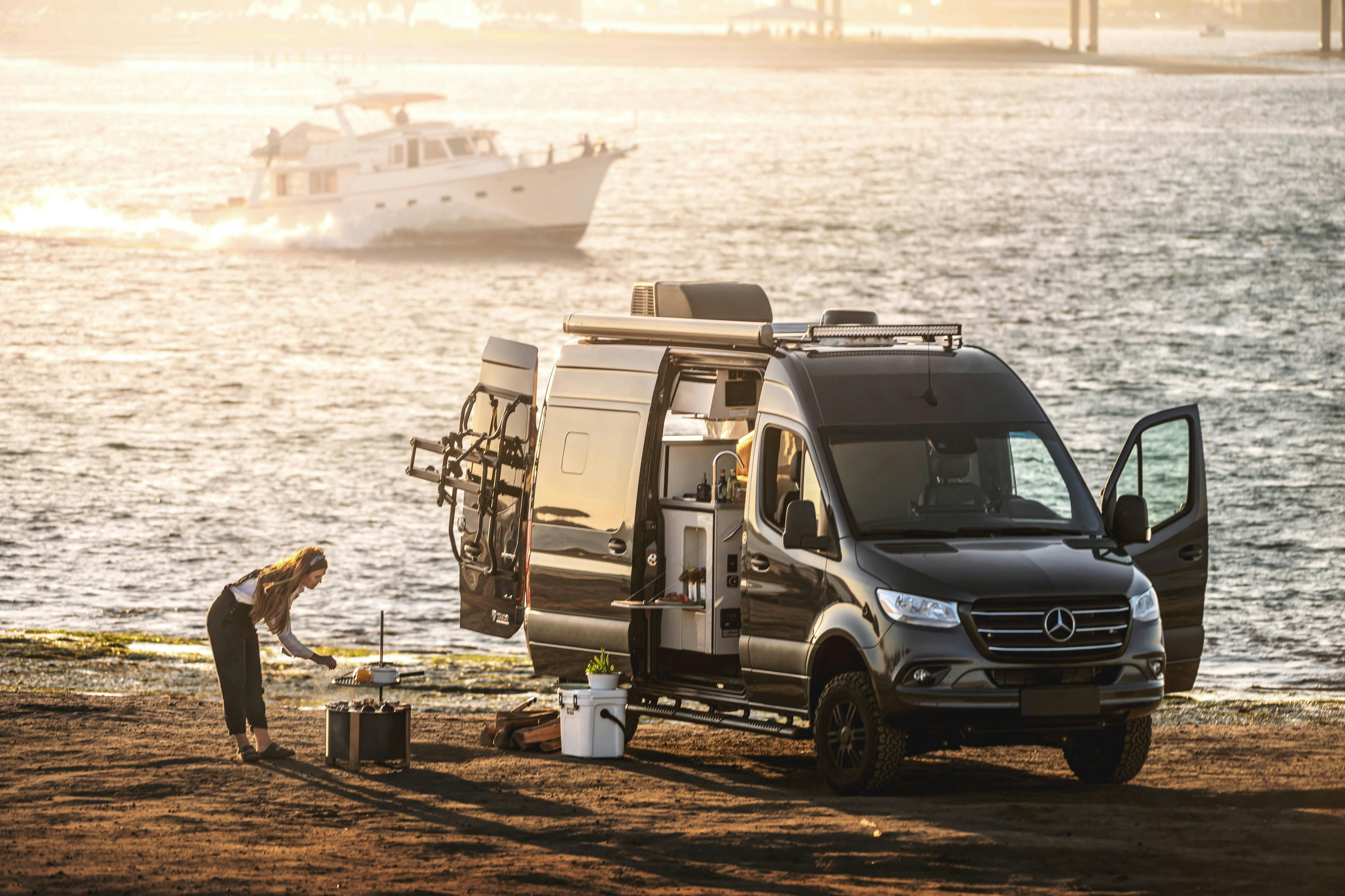 Sarah Glover cooking over an open fire next to the ocean and a TMC Tranquility camper van