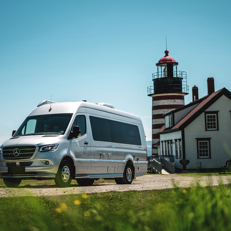 An Airstream Class B Van drives away from a lighthouse