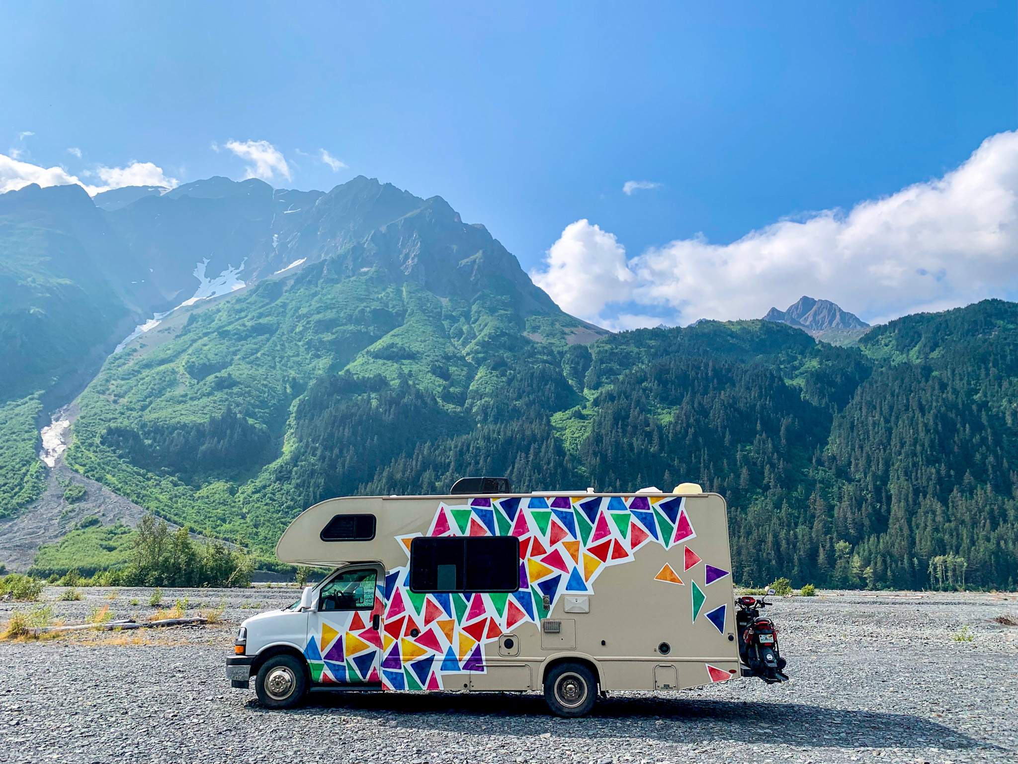Jason and Dawn's Class C RV parked in a gravel lot near a large mountain.