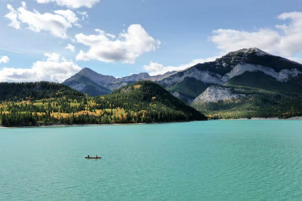 A couple kayaking on a pretty blue lake with mountains in the background.