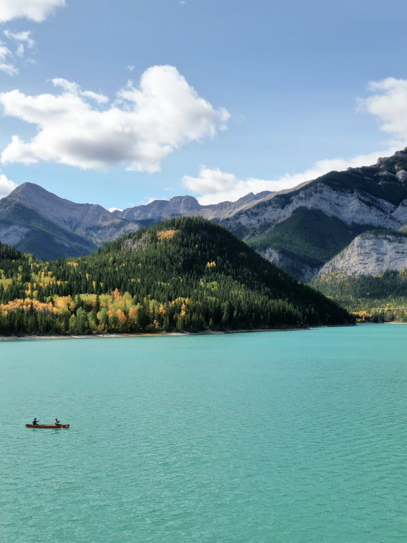 A couple kayaking on a pretty blue lake with mountains in the background.