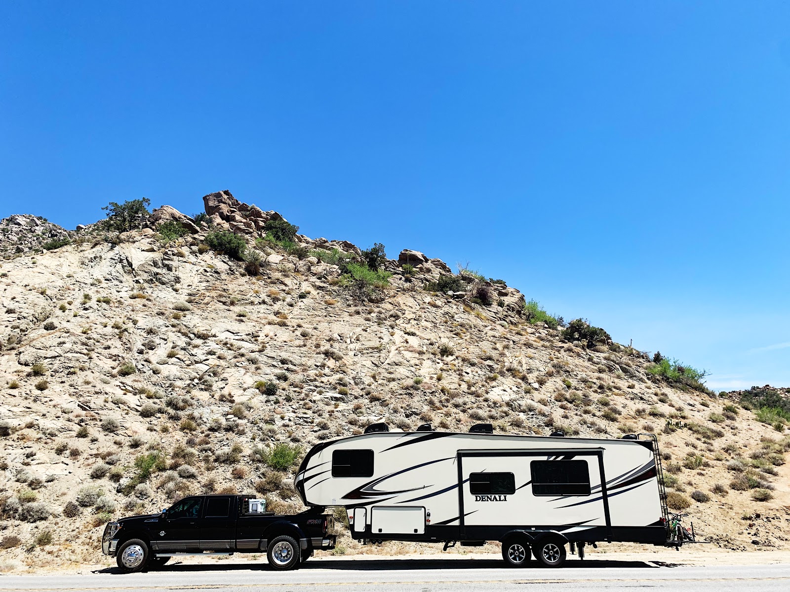 A truck towing an  RV parked in front of a sandy ridge.
