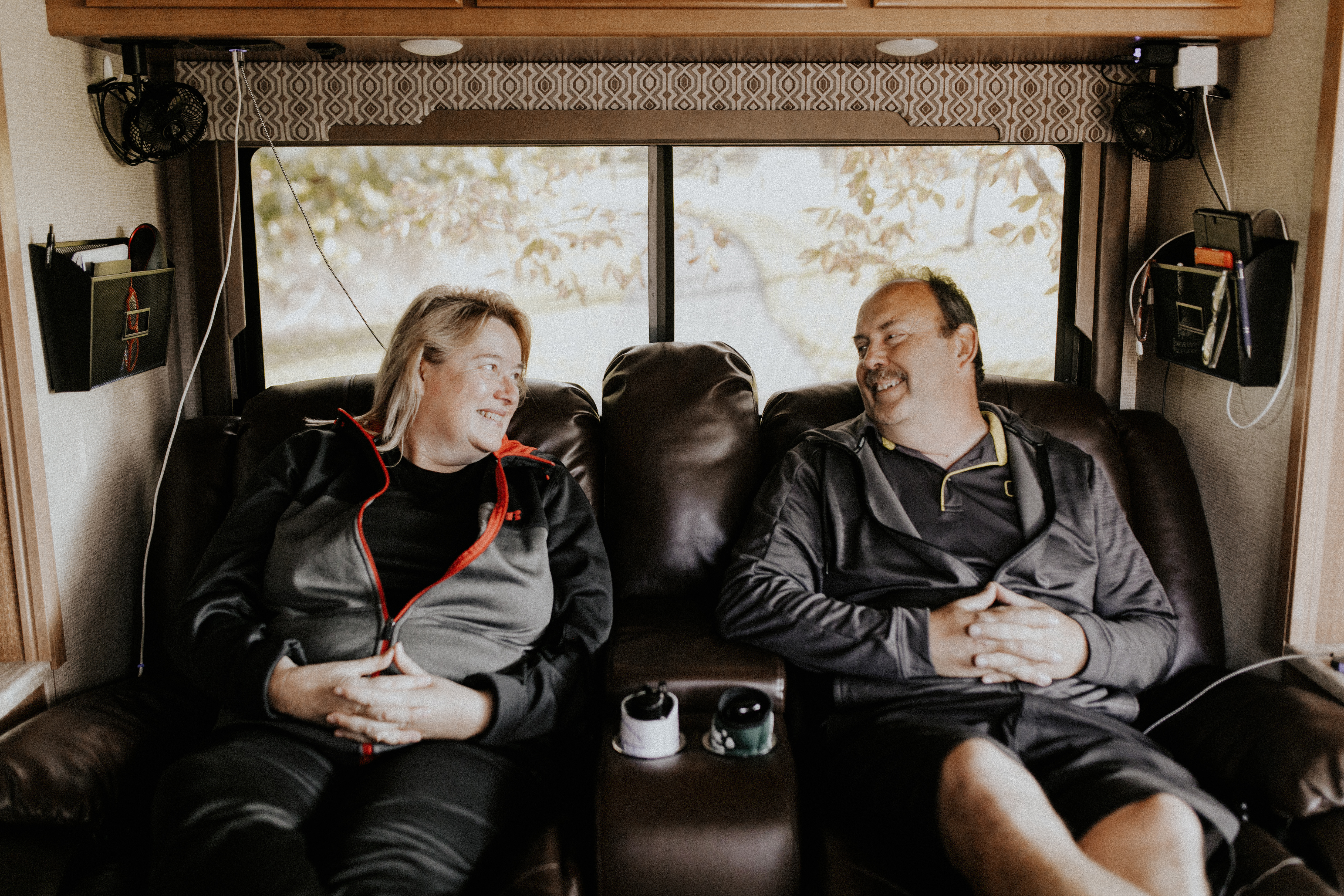 A middle-aged couple sitting in matching recliners inside their RV. 